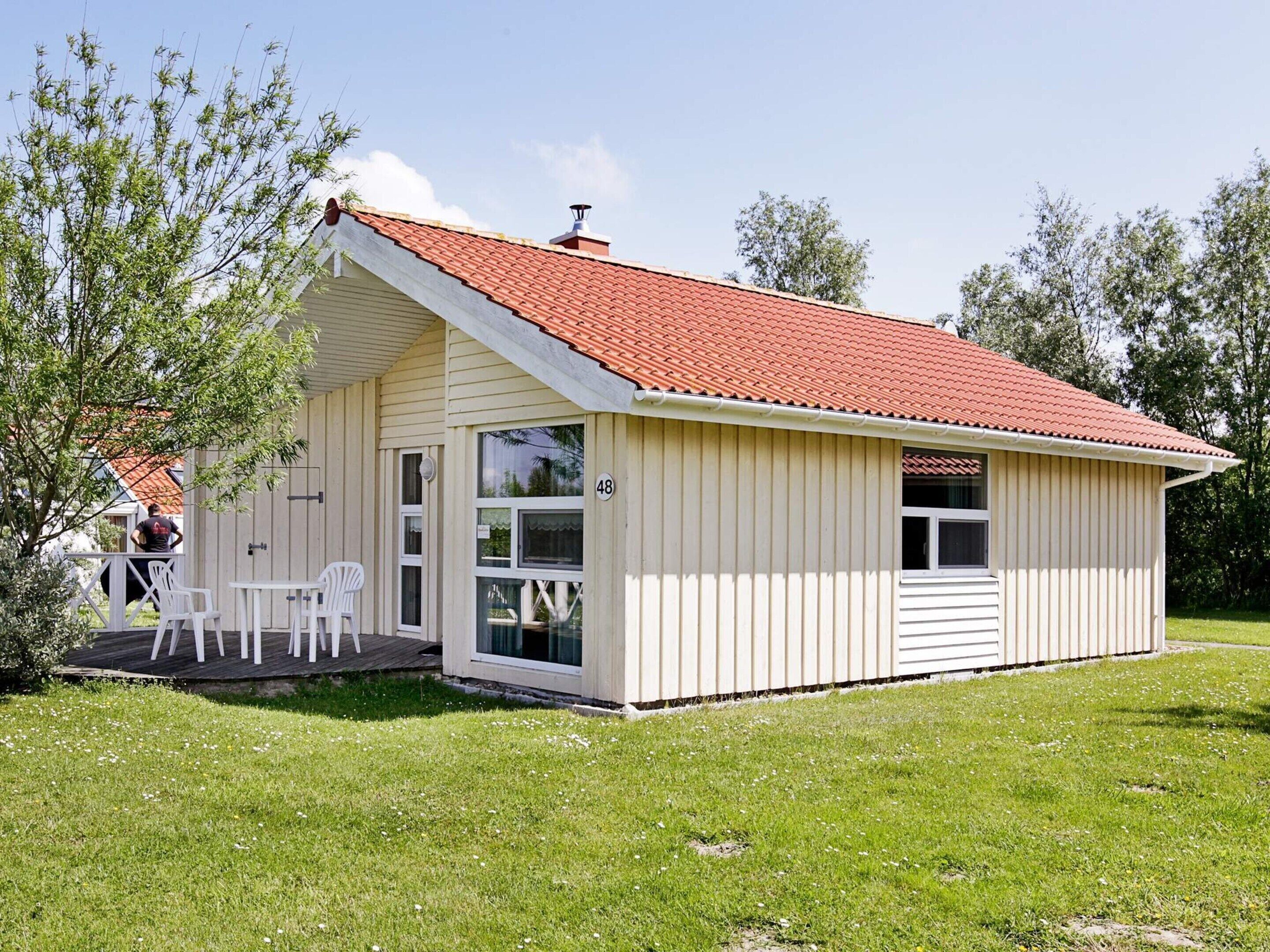 A small, single-story building with a red-tiled roof, a covered porch with white chairs, and a number '48' sign.