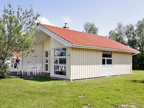 A small, single-story building with a red-tiled roof, a covered porch with white chairs, and a number '48' sign. - Holiday Home in Otterndorf (Otterndorf)