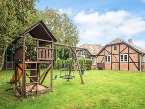 A playground with a wooden playhouse, swings, and a slide. - 4 Star Holiday Home in Hemmet (Hemmet)