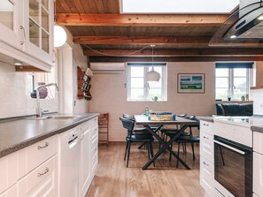 A modern kitchen with white cabinets, a wooden ceiling, a dining table with chairs, and a built-in oven. - 4 Star Holiday Home in Hemmet (Hemmet)