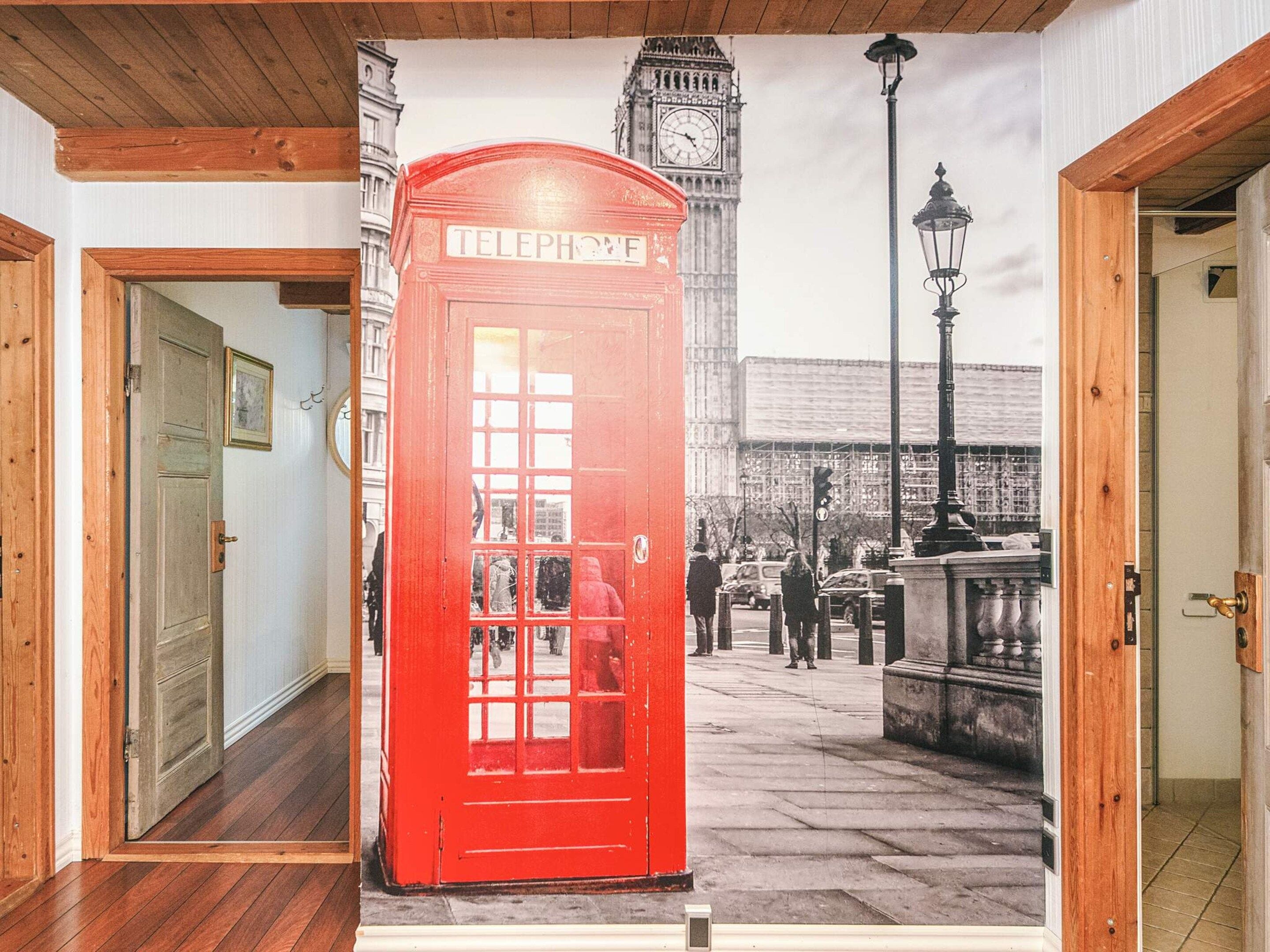 A room with a red telephone booth, a door, and a wall with a street scene mural.