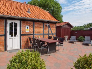 A brick building with a tiled roof, a white door, and a patio area with a table and chairs. - 4 Star Holiday Home in Hemmet (Hemmet)