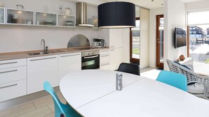 A modern kitchen with white cabinets, a stainless steel sink, and a built-in oven. There is a dining table with chairs and a large black pendant light. - 4 Person Holiday Home in Bogense-by Traum (Bogense)