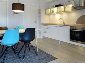A modern kitchen with white cabinets, a stainless steel oven, and a dining area with two chairs.