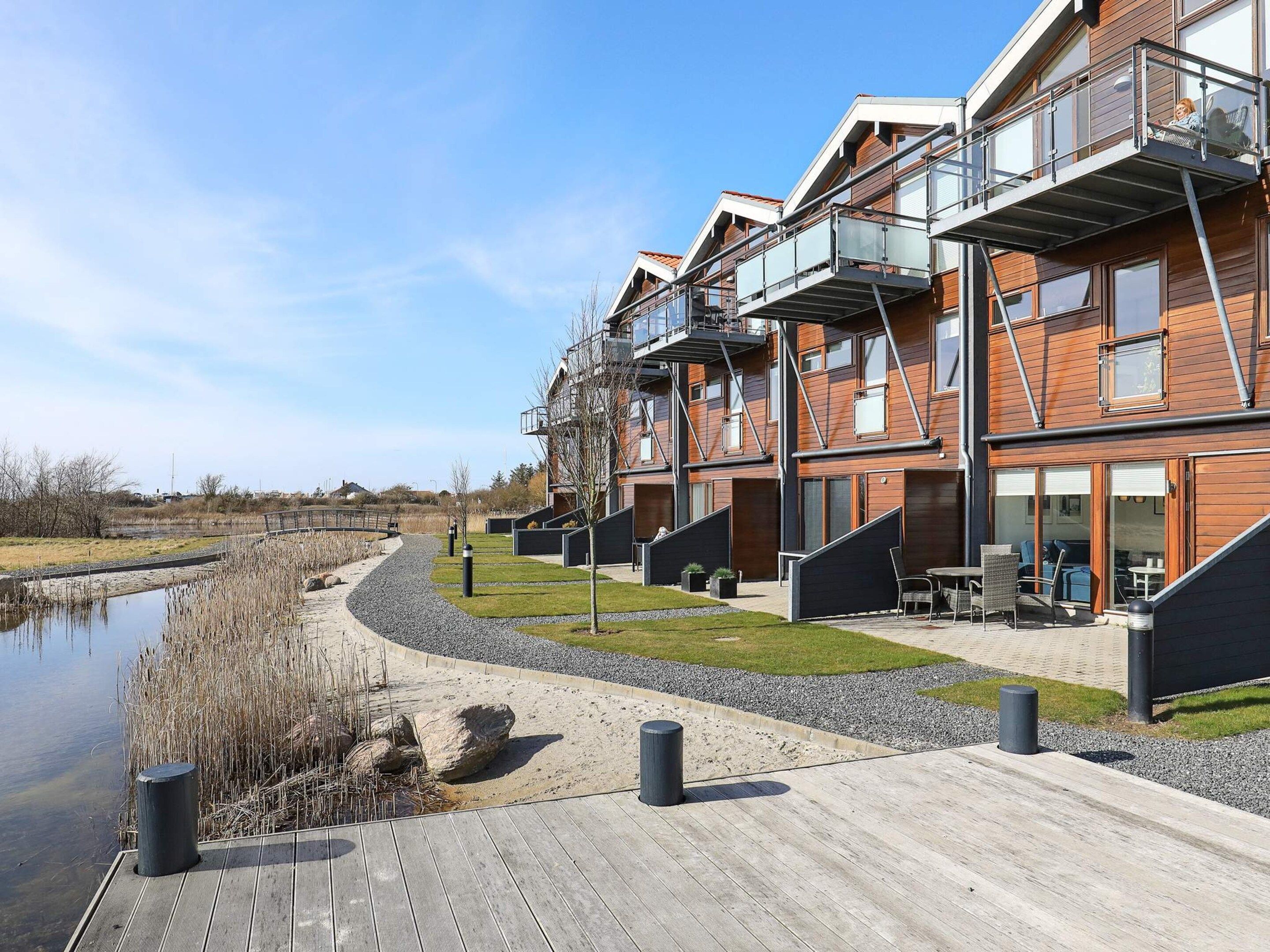 A modern residential building with a wooden facade, outdoor seating area, and a view of a water body.