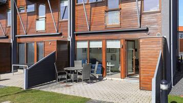 Ein modernes, mehrstöckiges Gebäude mit einer Terrasse, Sitzmöbeln und einem überdachten Sitzbereich.