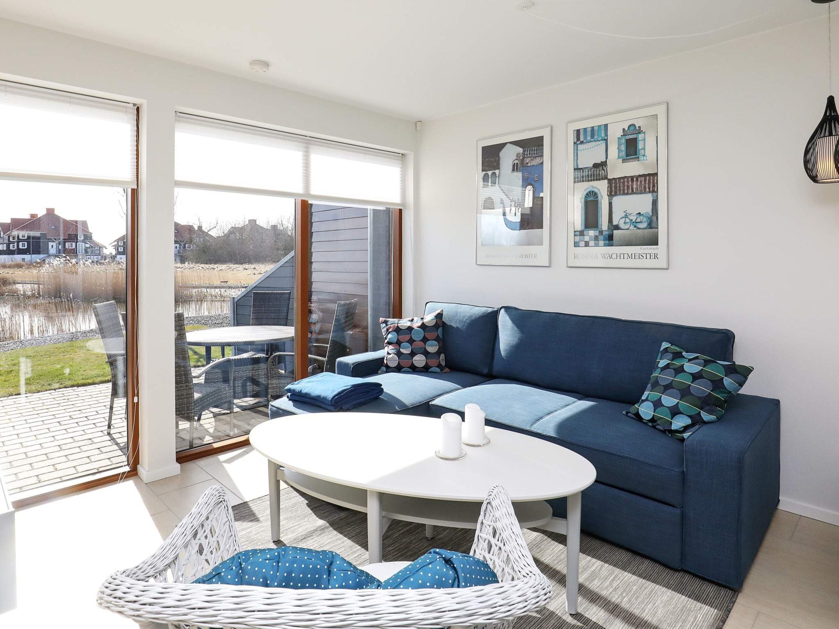 A modern living room with a blue sofa, a round white table, and wicker chairs.