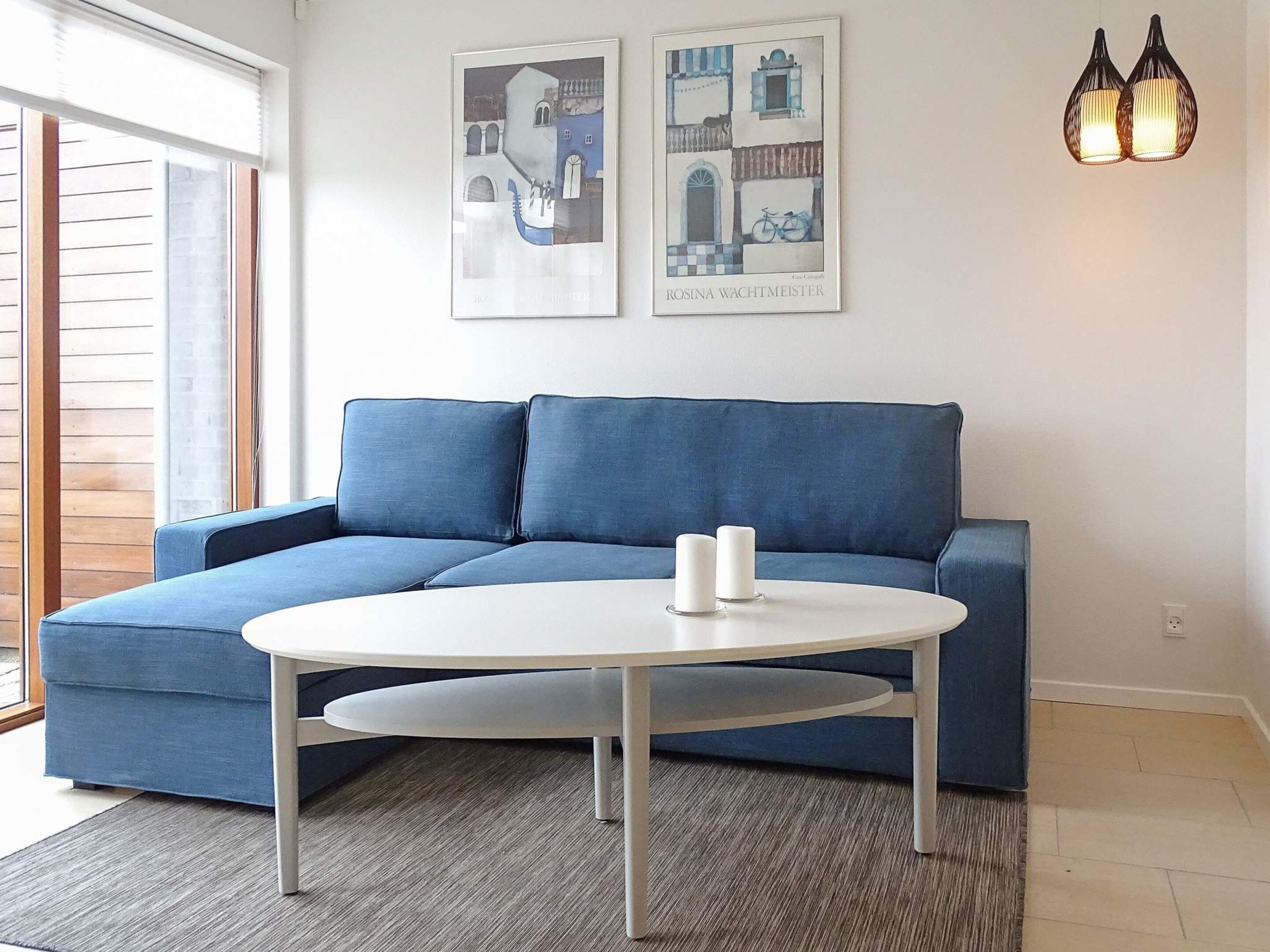 Una sala de estar moderna con un sofá azul, una mesa de centro blanca y dos obras de arte enmarcadas en la pared.