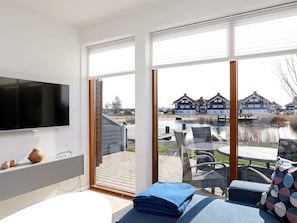 A modern room with a large TV, a bed, and a view of houses across a water body.