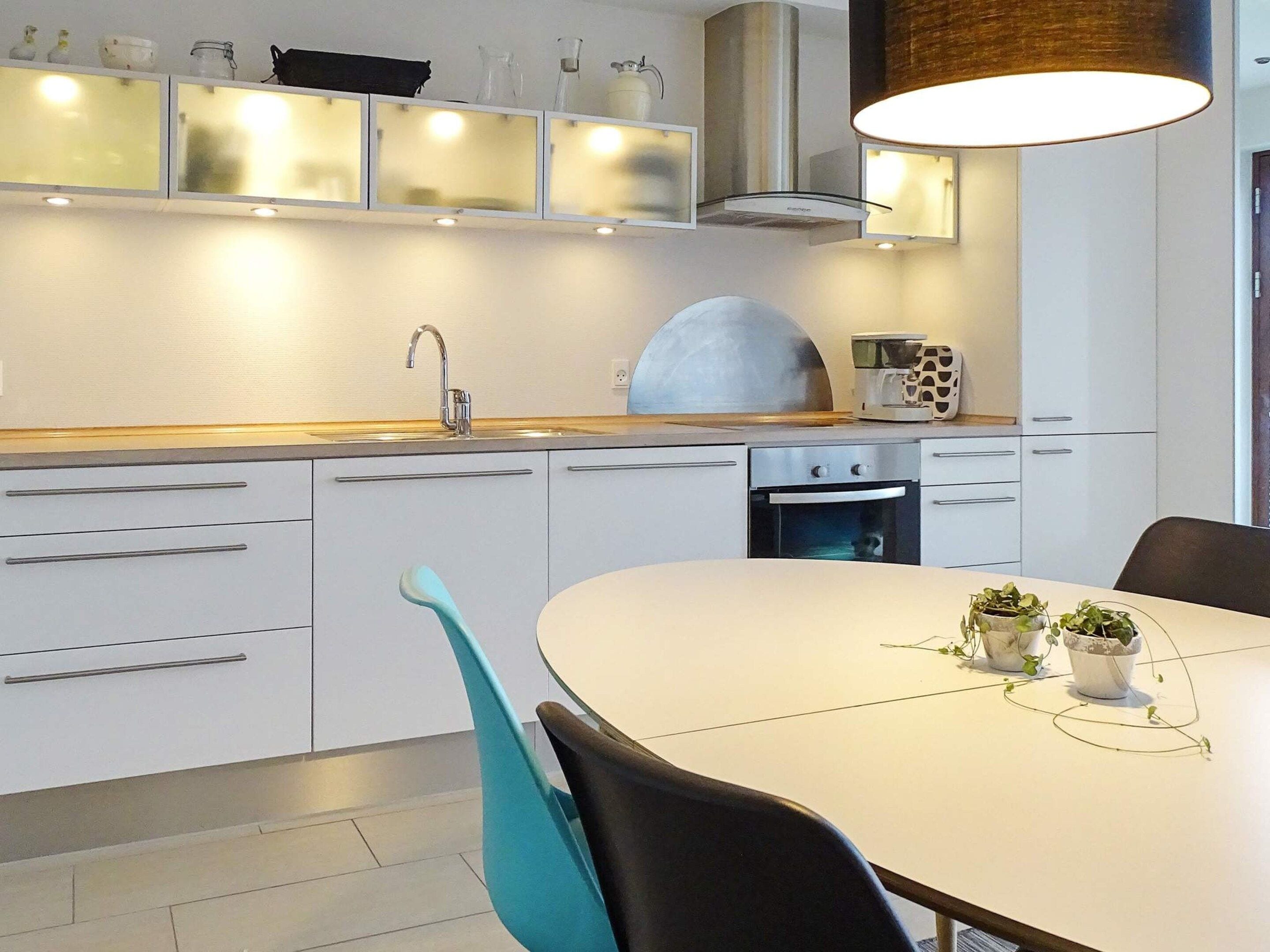 Une cuisine moderne avec un plan de travail blanc, des appareils en acier inoxydable et une table de salle à manger ronde, assortie de chaises.