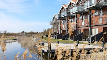 A modern residential building with balconies, a water body in front, and a clear sky.