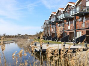 A modern residential building with balconies, a water body in front, and a clear sky.