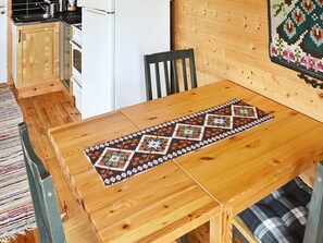 A wooden dining table with a geometric-patterned runner, a black chair, and a kitchen area with a refrigerator and cabinets. - 3 Person Holiday Home in Hitra (Hitra)