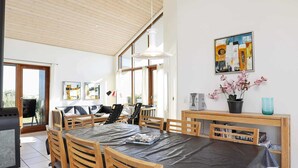 Een ruime eetruimte met een grote tafel, houten stoelen en een barbecue buiten.