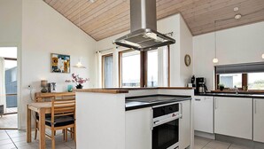 Een moderne keuken met witte kasten, een centraal eiland met een fornuis, en een groot raam dat voor natuurlijk licht zorgt.