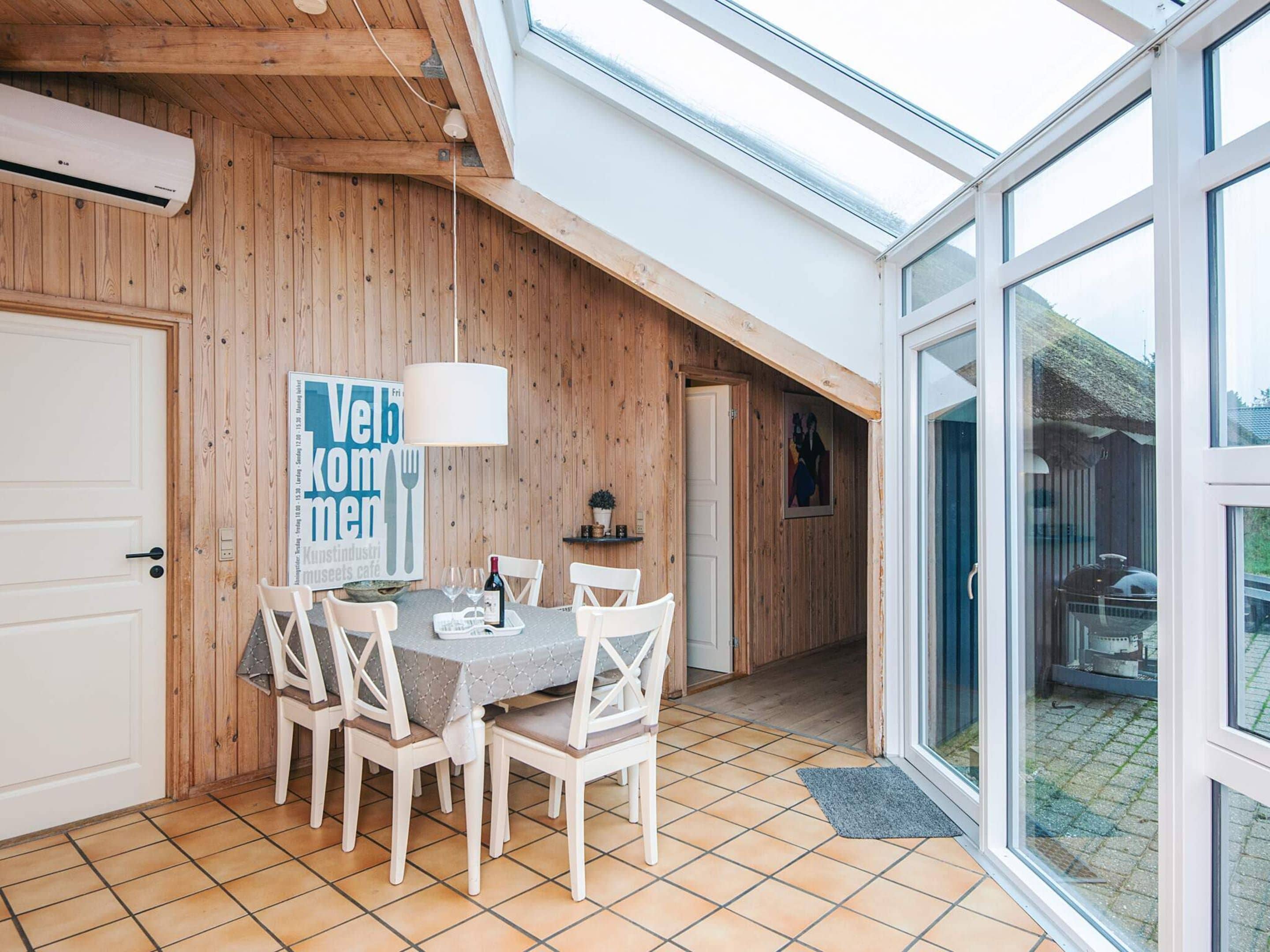 A dining area with a table set for four, wooden walls, a large window, and a door.
