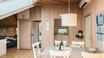 A cozy wooden interior with a dining area featuring a table and chairs, a kitchen with a window, and a living area with a sofa.