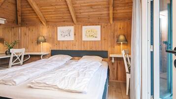A cozy bedroom with a wooden ceiling, a bed with white linens, two bedside tables with lamps, and a window with curtains.
