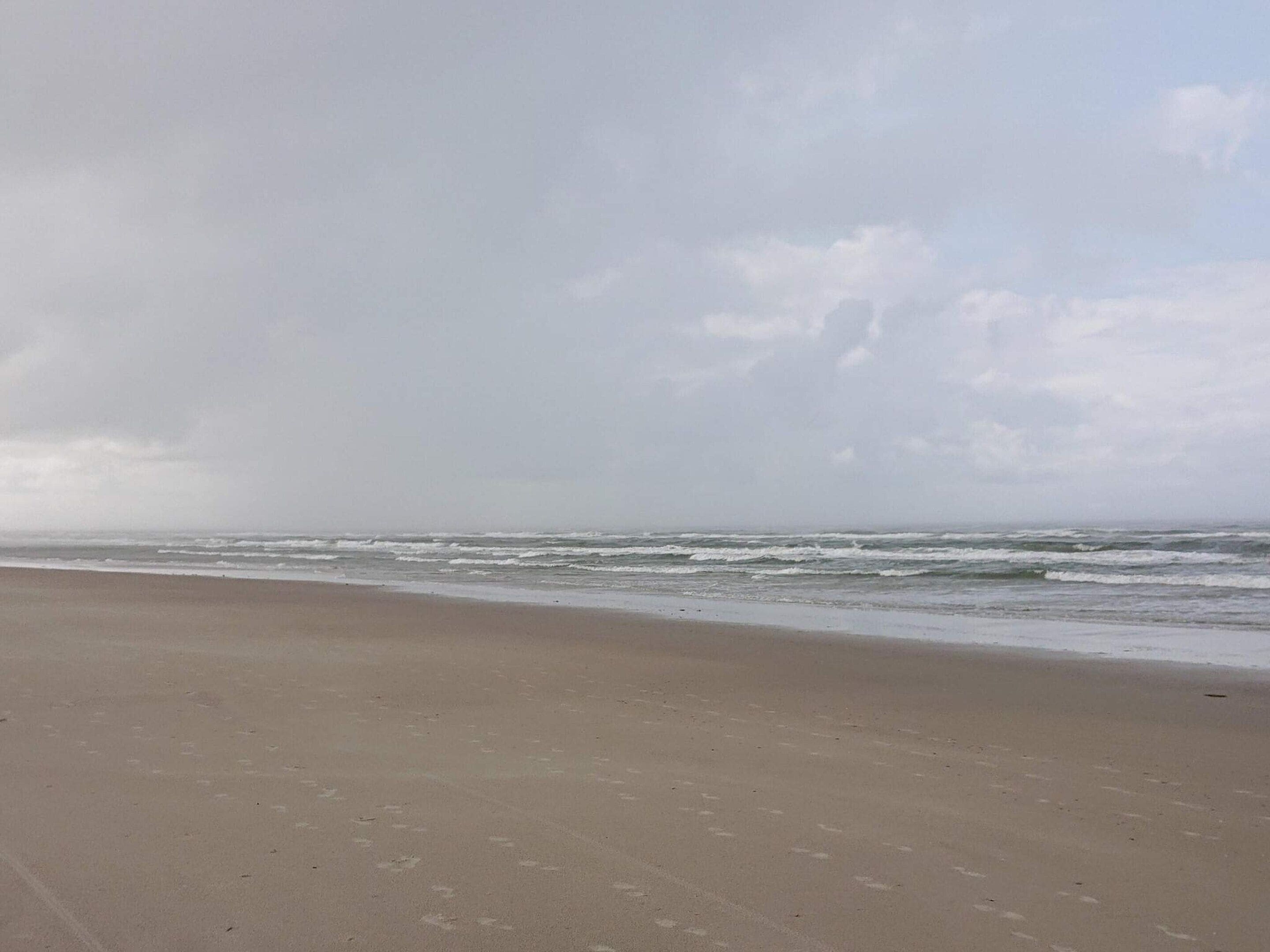 A beach with a wide sandy shore and waves approaching the beach.