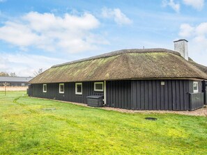 A thatched-roof building with a flat roof, a chimney, and a small attached structure with a window. - Beautiful Holiday Home in Vejers Strand with Hot Tub (Vejers Strand)