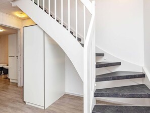 Staircase leads to an upper level, with a wardrobe and seating area nearby.