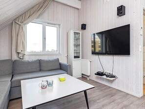 A modern living room with a grey sofa, a white coffee table with mugs, a flat-screen TV mounted on the wall, and a cabinet with glass doors. - Holiday Home in Wendtorf (Wendtorf)