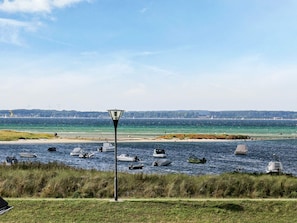 A coastal view with boats on the water, a lamp post, and a distant shoreline with wind turbines.