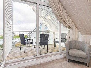 A balcony with a view of a beach, a sliding glass door, and a grey armchair. - Holiday Home in Wendtorf (Wendtorf)