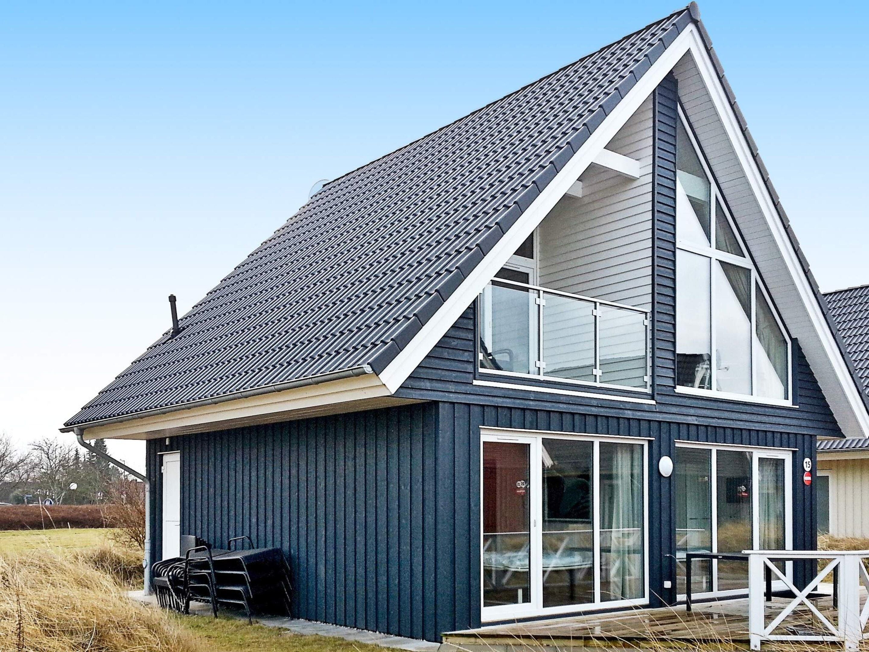 A modern two-story house with a steeply pitched roof, large windows, and a covered outdoor seating area.