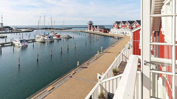 Un puerto deportivo con barcos amarrados, un muelle y edificios rojos con detalles blancos.