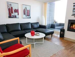 A modern living room with a black leather sofa, a wooden chair with a red cushion, a white coffee table, and a fireplace. - 8 Person Holiday Home in Hadsund-by Traum (Hadsund)