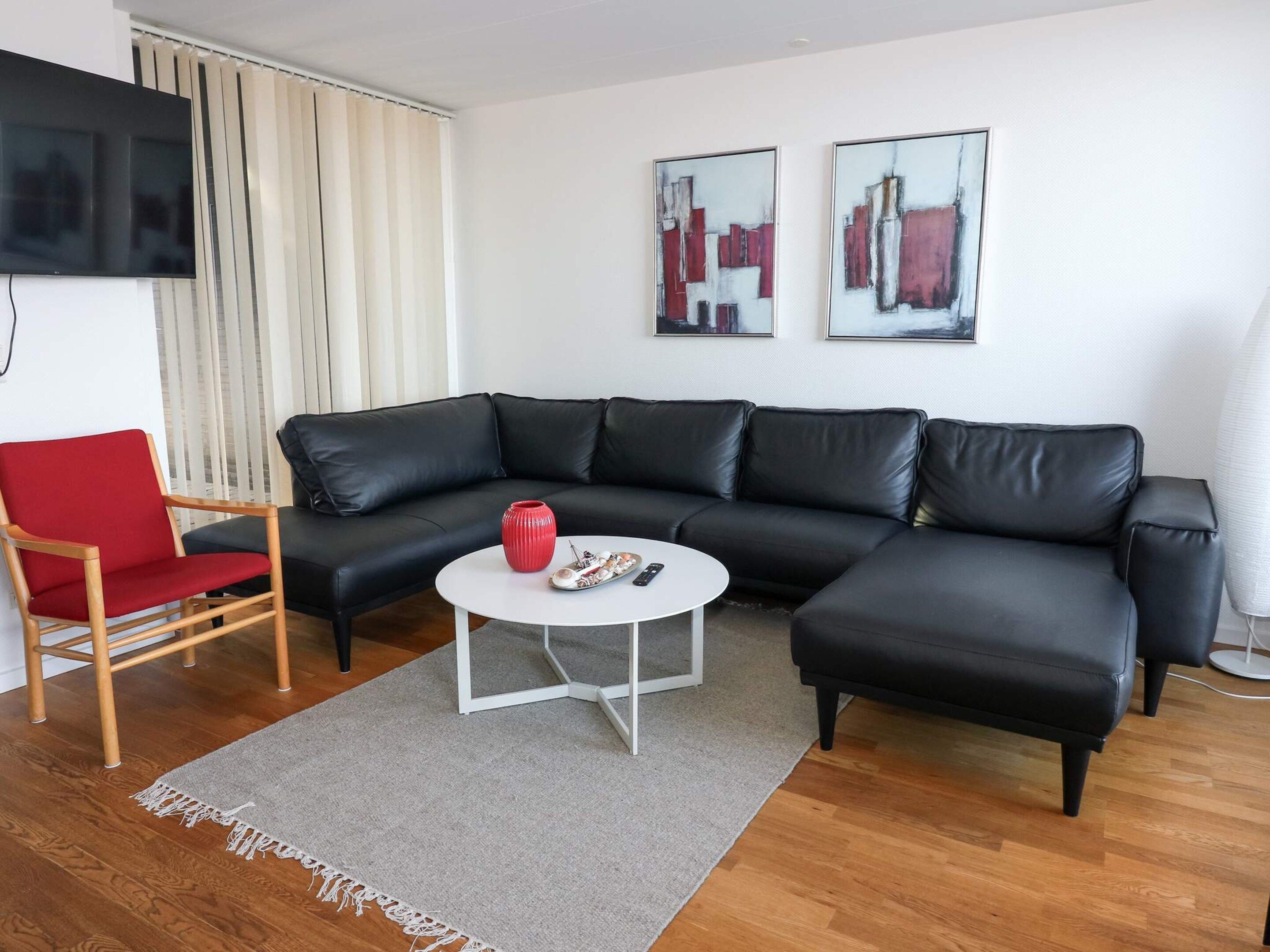 A modern living room with a black leather sofa, a red chair, a white coffee table, and two abstract paintings on the wall.