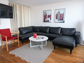 Una sala de estar moderna con un sofá de cuero negro, un sillón rojo, una mesa de centro blanca y dos cuadros abstractos en la pared.