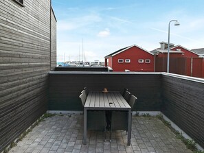 Un patio con una mesa y sillas, un edificio rojo al fondo y vistas de barcos.