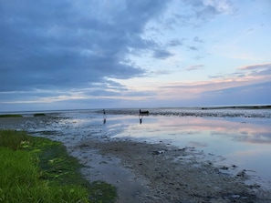 Ein Strand mit zwei Personen, ruhigem Wasser und bewölktem Himmel.