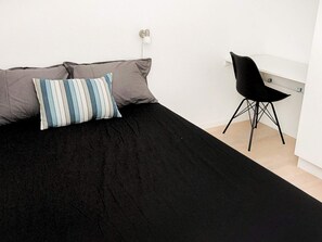 A bed with a black cover and two pillows, a black chair, and a white desk in a room with white walls. - 8 Person Holiday Home in Hadsund-by Traum (Hadsund)