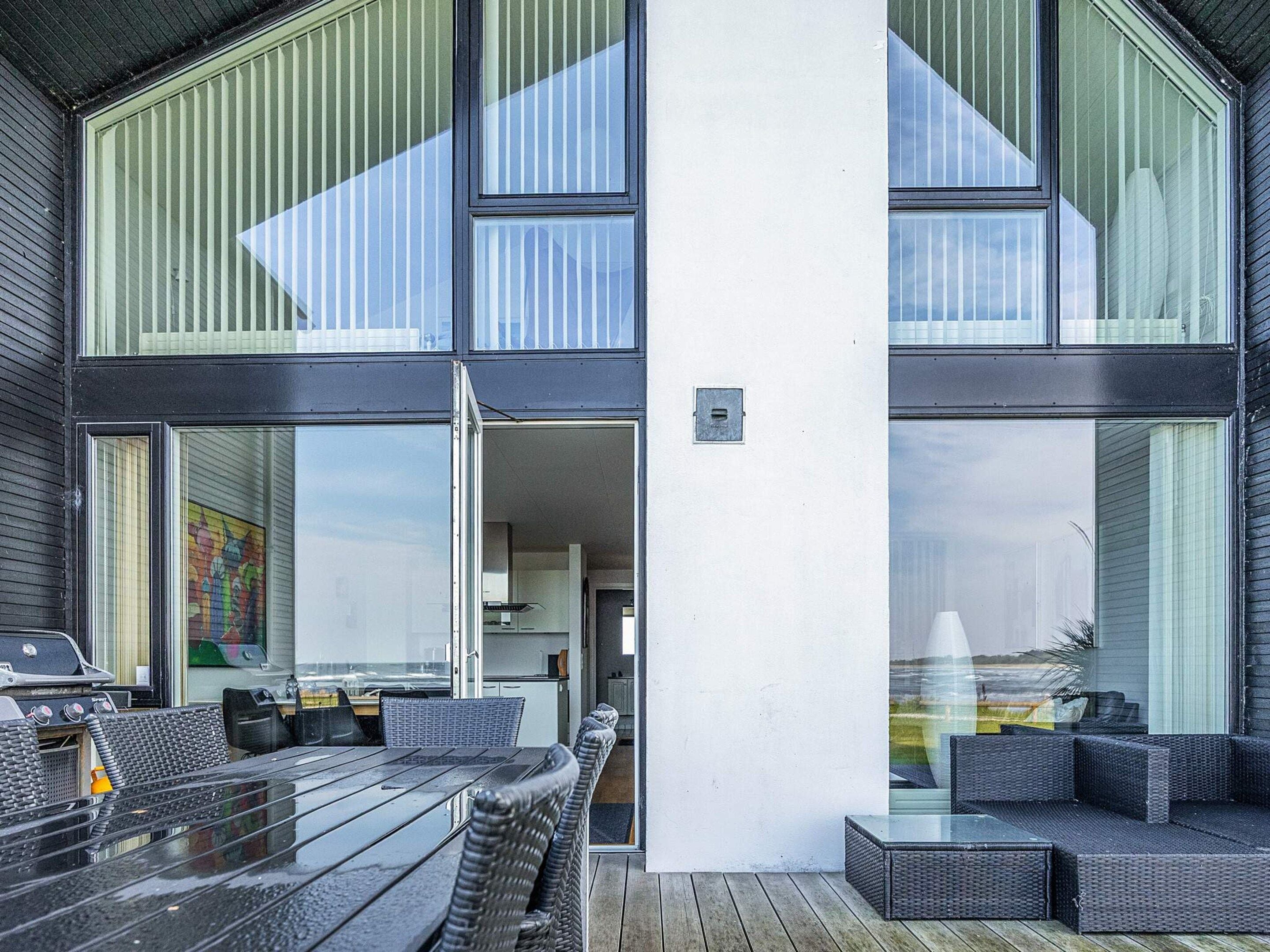 A modern outdoor seating area with a wooden deck, a glass partition, and a view of the sea.