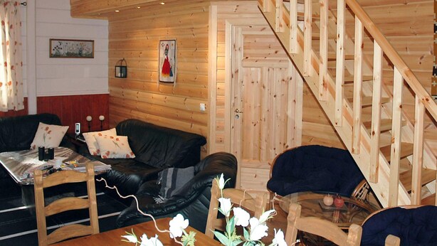 A wooden interior with a staircase, a black leather sofa, a wooden dining table, and a glass coffee table. - Holiday Home in Isfjorden (Rauma)
