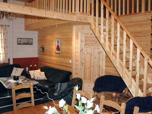 A wooden interior with a staircase, a black leather sofa, a wooden dining table, and a glass coffee table. - Holiday Home in Isfjorden (Rauma)