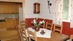 A wooden dining table with chairs, a vase with flowers, a wall-mounted light fixture, and a window with curtains. - Holiday Home in Isfjorden (Rauma)