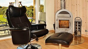 Ein modernes Interieur mit einem Ledersessel, einem Glastisch und einem Kaminofen.