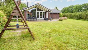 Ein Haus mit einer überdachten Terrasse, einer Holzleiter und einem Rasen.