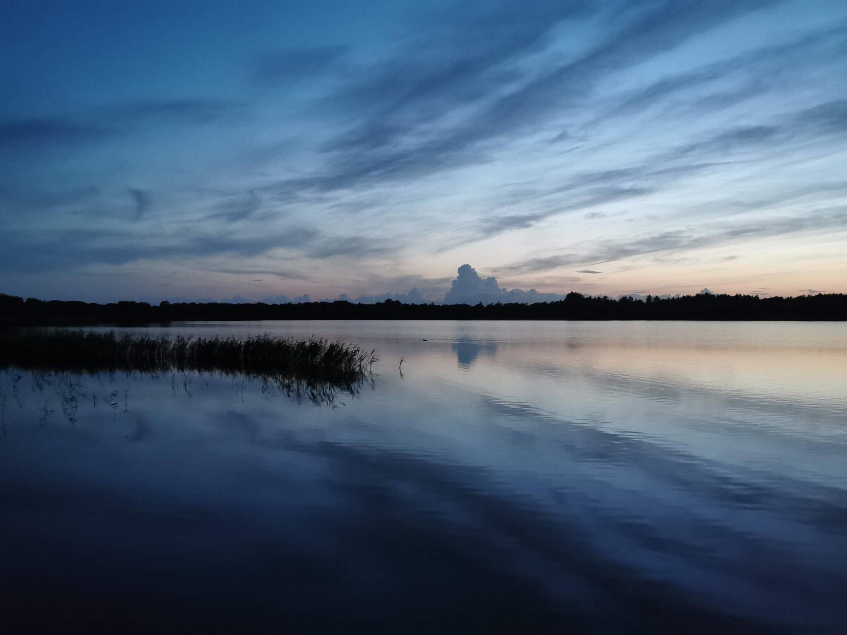 A calm body of water reflecting the sky with a horizon line and distant trees.