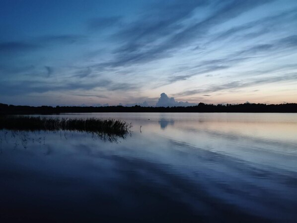 A calm body of water reflecting the sky with a horizon line and distant trees.