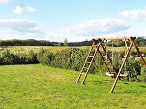 A wooden swing set in a grassy field with a clear sky.
