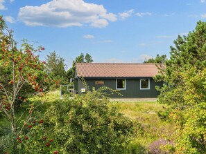 A single-story building with a dark exterior and a red-tiled roof, surrounded by dense greenery and trees.