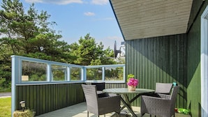 Une terrasse extérieure couverte, avec une table et des chaises, un pot de fleurs et une antenne parabolique.