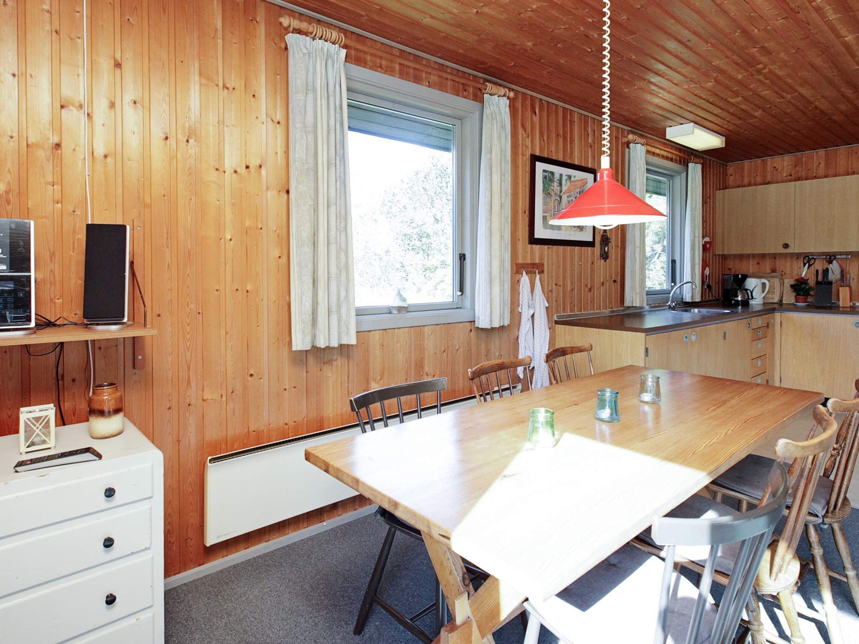 A wooden-paneled room with a dining table, chairs, a white cabinet, and a kitchen area with a sink and stove.