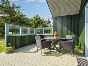 A covered outdoor patio with a table and chairs, a potted plant, and a view of the surrounding greenery.