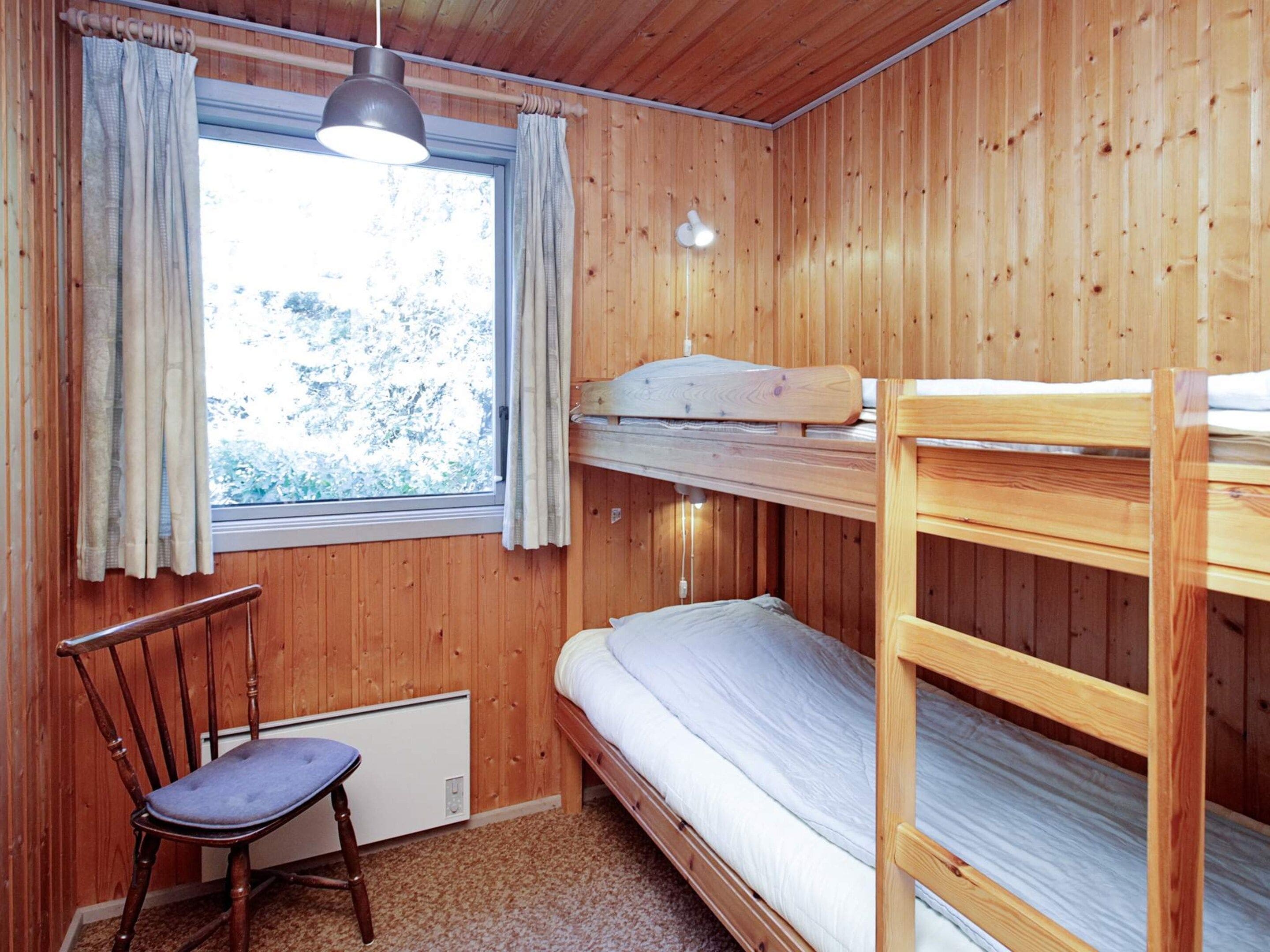 Une pièce en bois avec des lits superposés, une chaise, une fenêtre avec des rideaux et un luminaire suspendu.